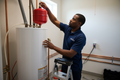 black-plumber-in-navy-polo-that-says-metro-installing-expansion tank on top of water-heater